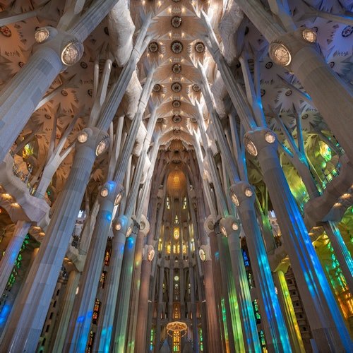 Intrincadas columnas y coloridas vidrieras en el interior de una gran catedral abovedada con elaborados detalles en el techo.