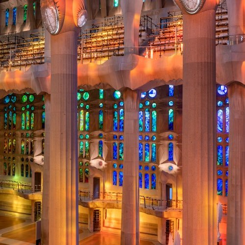 Altas columnas y coloridas vidrieras en el interior de un gran edificio ornamentado con balcones iluminados con luces cálidas y frías.