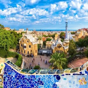 Colorful tiled mosaic foreground, people walking below, unique gingerbread-like buildings, and a cityscape under a partly cloudy sky.