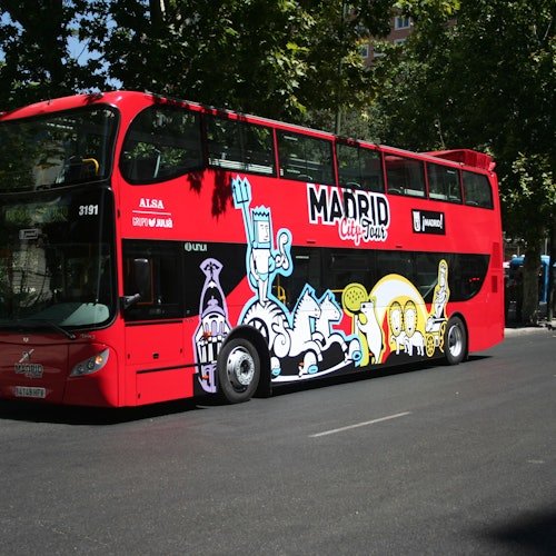 Autobús rojo de dos pisos con la marca "Madrid City Tour" e ilustraciones de dibujos animados de colores en el lateral, aparcado en una calle.