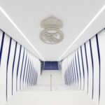 A white and blue hallway with striped walls and a ceiling emblem, leading to stairs in the distance.