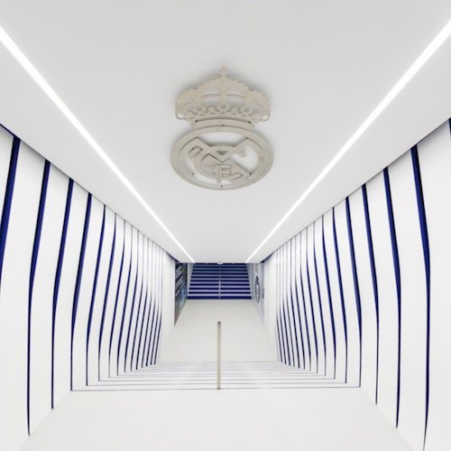 A white and blue hallway with striped walls and a ceiling emblem, leading to stairs in the distance.
