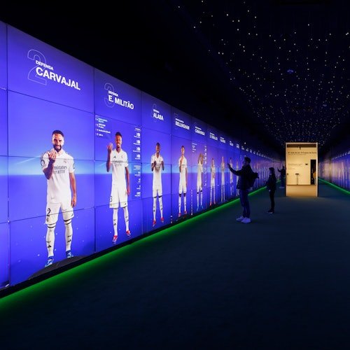 A futuristic display wall showing life-sized images of soccer players in a dimly lit room with visitors interacting.