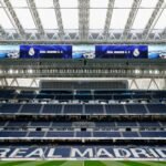 A view of an empty stadium with "Real Madrid C.F." displayed on large screens and "Real Madrid" written on the seating.