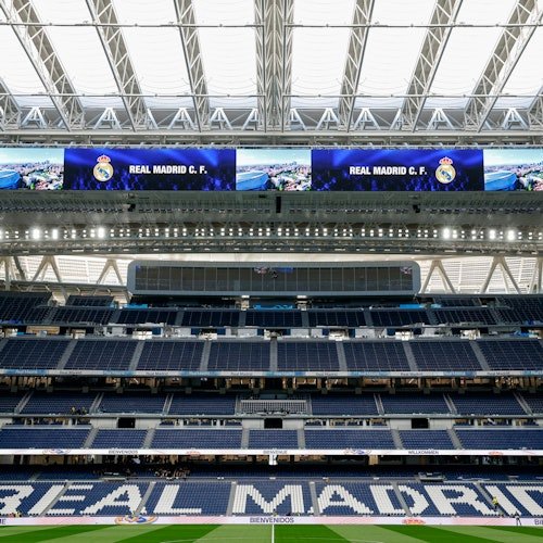 A view of an empty stadium with "Real Madrid C.F." displayed on large screens and "Real Madrid" written on the seating.