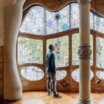 Una persona con auriculares está de pie dentro de una habitación con grandes vidrieras de colores y marcos de madera ornamentados.