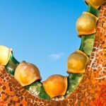 Detalle arquitectónico curvo con macetas de cerámica amarilla y azulejos de mosaico contra un cielo azul claro.