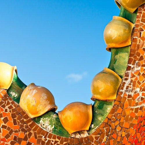 Detalle arquitectónico curvo con macetas de cerámica amarilla y azulejos de mosaico contra un cielo azul claro.